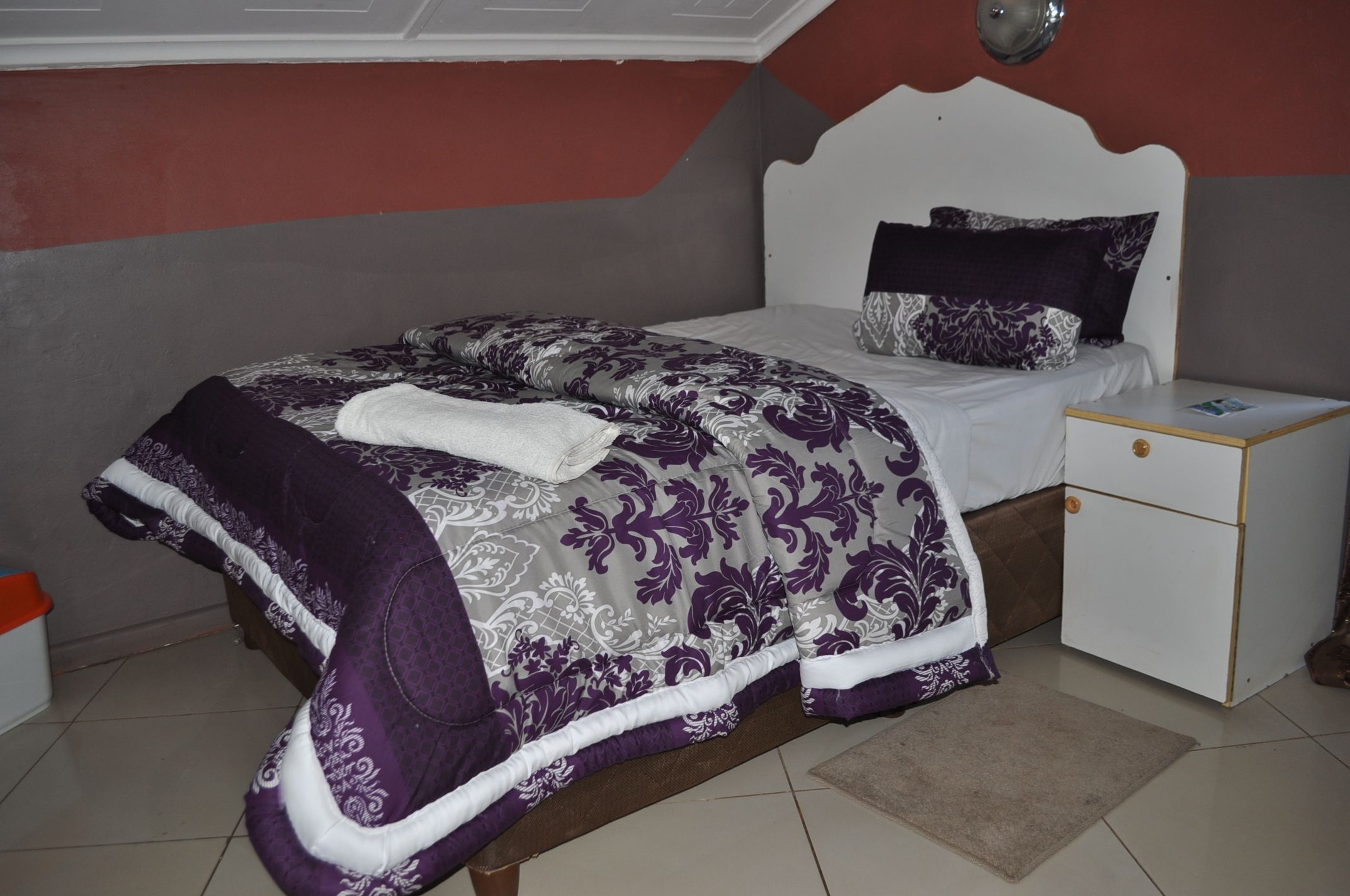 A bedroom with a bed, nightstand, and a wall-mounted light fixture.