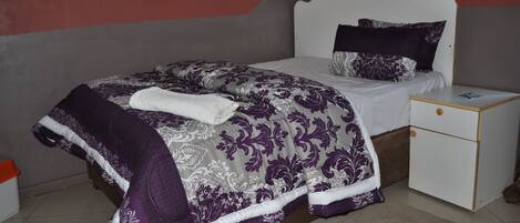 A bedroom with a bed, nightstand, and a wall-mounted light fixture.