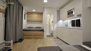 A compact bedroom with a bed, a small kitchenette, and a bathroom. - Apartment 1 - FREE Ride cabins (Tösens)