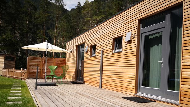 A wooden cabin with a deck, a covered outdoor seating area, and a door with a window. - Apartment 1 - FREE Ride cabins (Tösens)