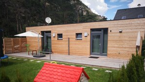 A wooden cabin with a deck, a satellite dish, and a small playhouse in the foreground. - Apartment 1 - FREE Ride cabins (Tösens)