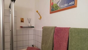 Ett badrum med dusch, en handduksställning med flera handdukar, en tvålkopp och en liten hylla med en dekorativ prydnad.