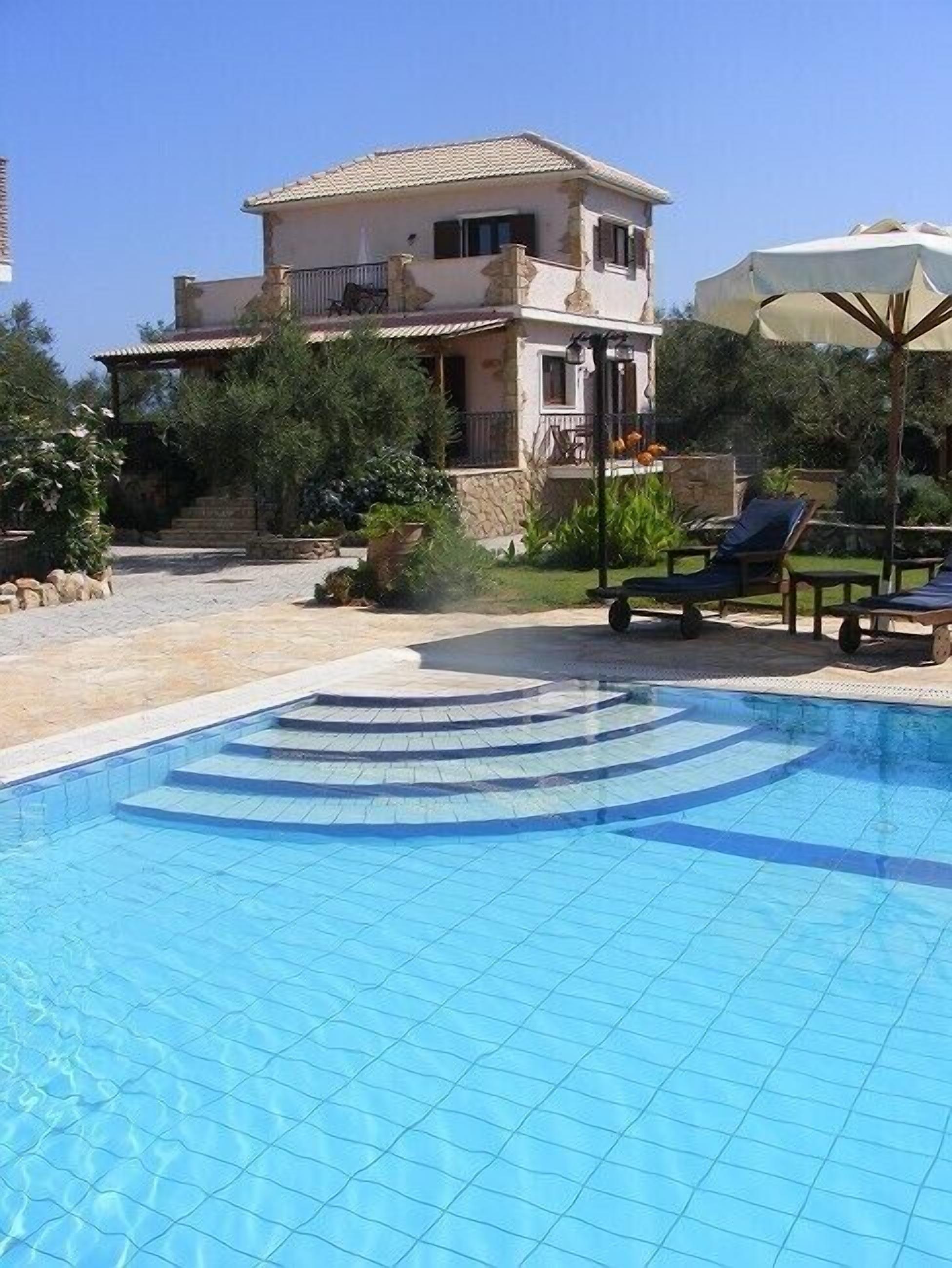 A swimming pool with steps leading into it, surrounded by lounge chairs and a building with a balcony.