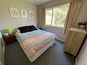 A bedroom with a bed, a nightstand, a window with curtains, and a wooden cabinet.