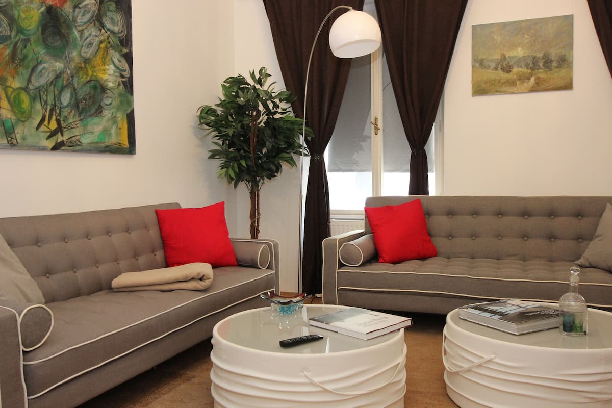 A living room with two grey sofas, red cushions, a glass coffee table, a plant, and artwork on the walls.