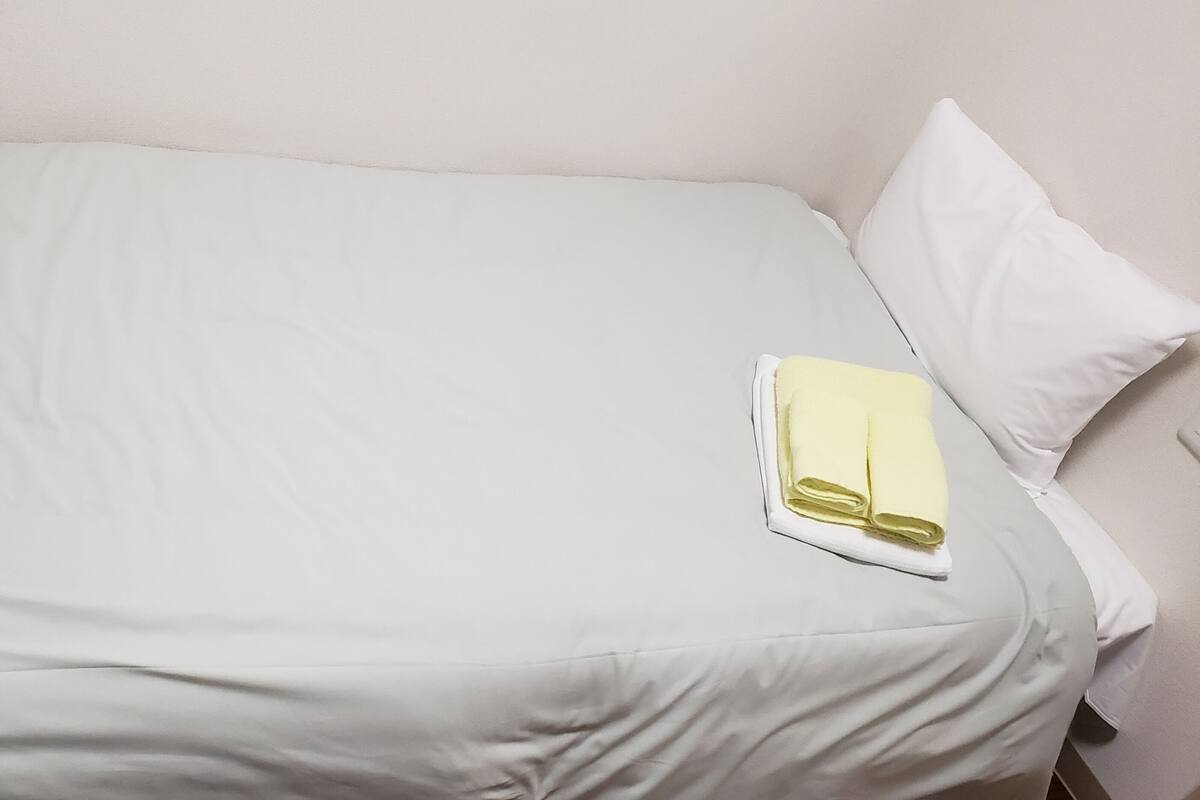 A neatly made bed with white bedding and a folded towel on the side.