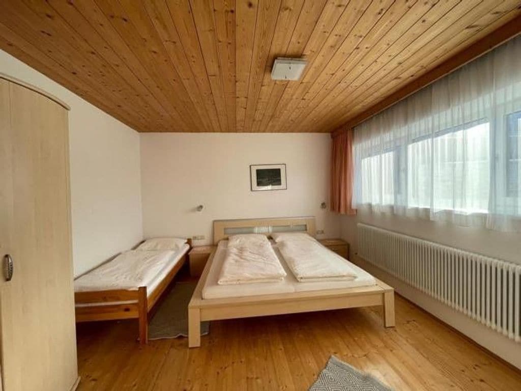 Une chambre avec deux lits en bois, un radiateur et une fenêtre avec des rideaux.