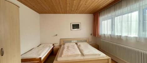 A room with two wooden beds, a radiator, and a window with curtains.