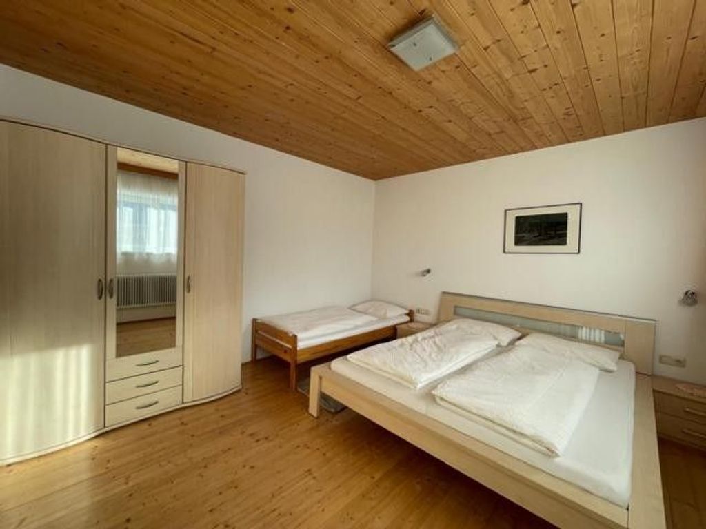 A bedroom with two single beds, a wooden wardrobe, and a small window.