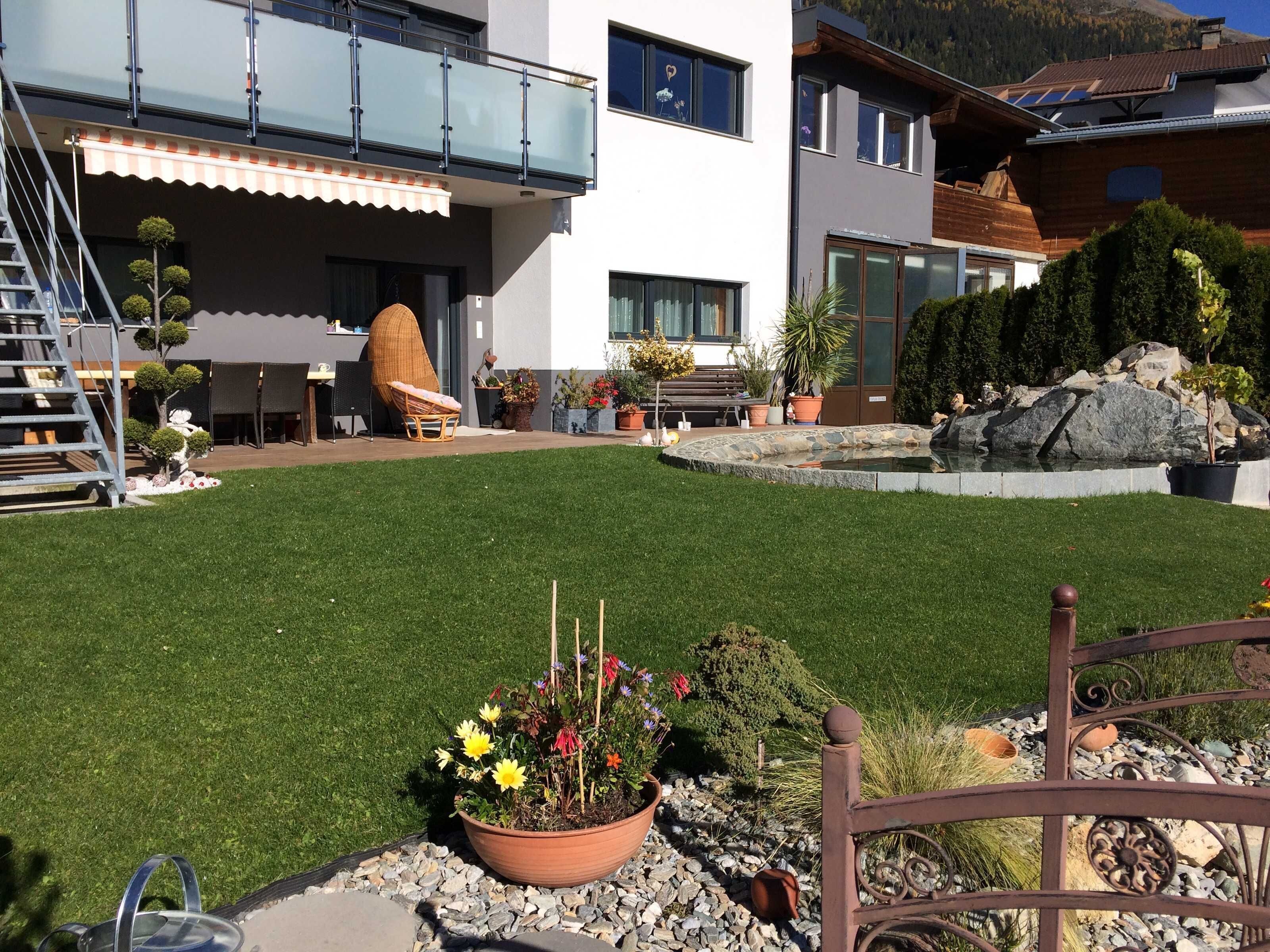 A modern house with a well-maintained lawn, outdoor seating, and a stone fountain.
