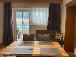 A room with a wooden table, two chairs, a sofa, and a view of the beach through a window.