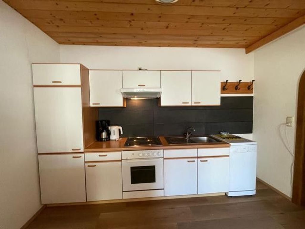 A compact kitchen with white cabinetry, a stove, a sink, and a dishwasher.