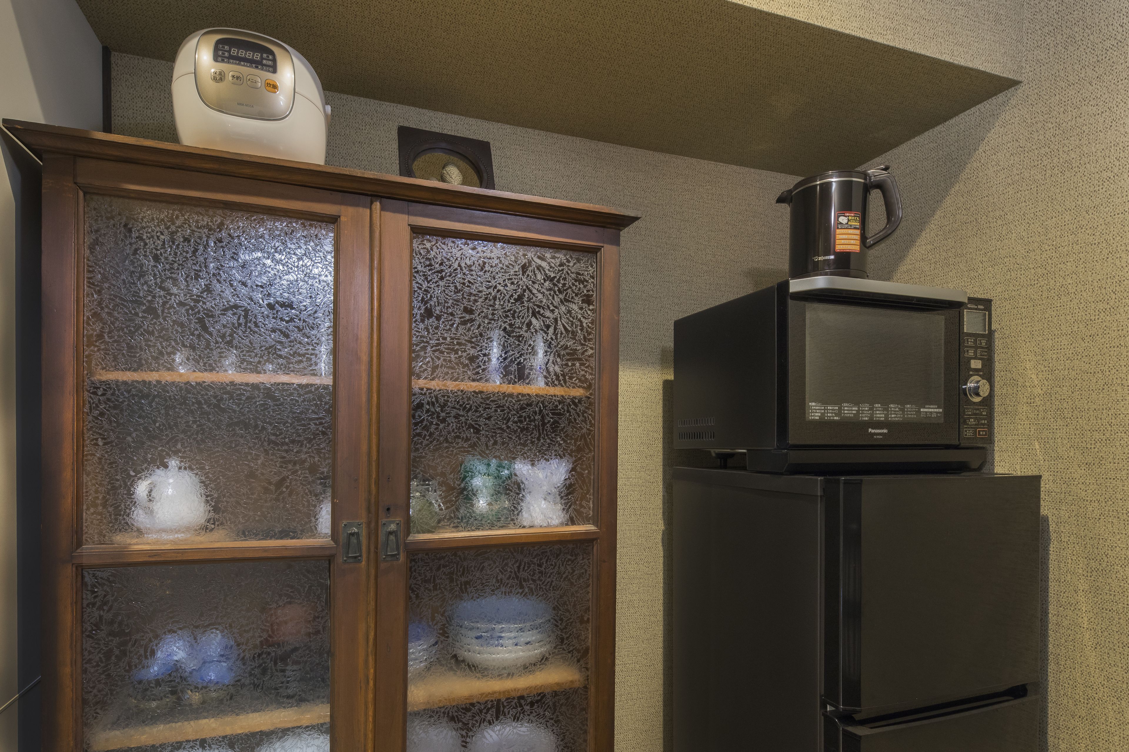 Una cocina con un microondas encima del refrigerador, un mueble con puertas de vidrio y un reloj en la pared.