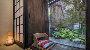 Ett traditionellt japanskt rum med tatamimattor på golvet, en låg träbänk med kuddar, en shojiskärm och en liten trädgård inomhus.