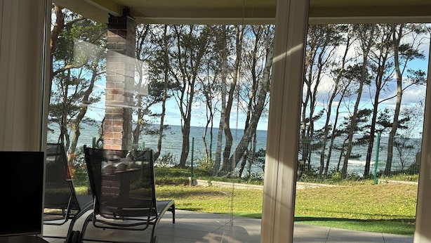 Una habitación con puerta de vidrio que da a un patio con vistas al mar y a árboles.