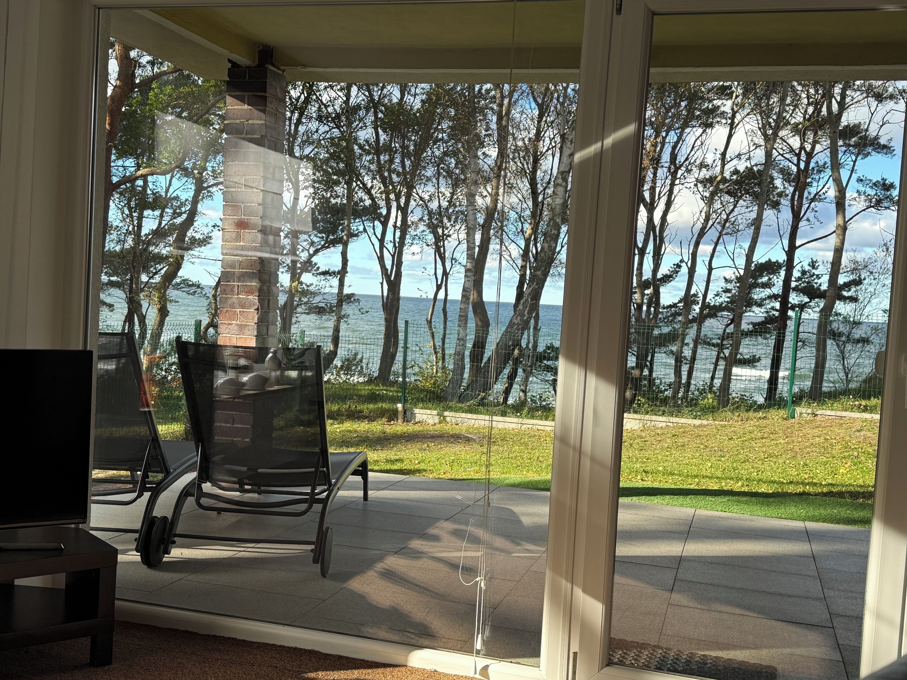 A room with a glass door leading to a patio with a view of the sea and trees.