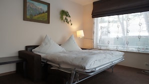 Una habitación de hospital con una cama, una mesita de noche, una lámpara, una ventana con cortinas y un cuadro en la pared.