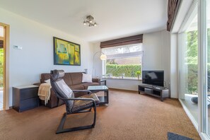 A modern living room with a sofa, a recliner, a coffee table, a TV, and a large window with a view of greenery. - Vacation bungalow with a stunning ocean view for 2 to 4 people, (Pobierowo)