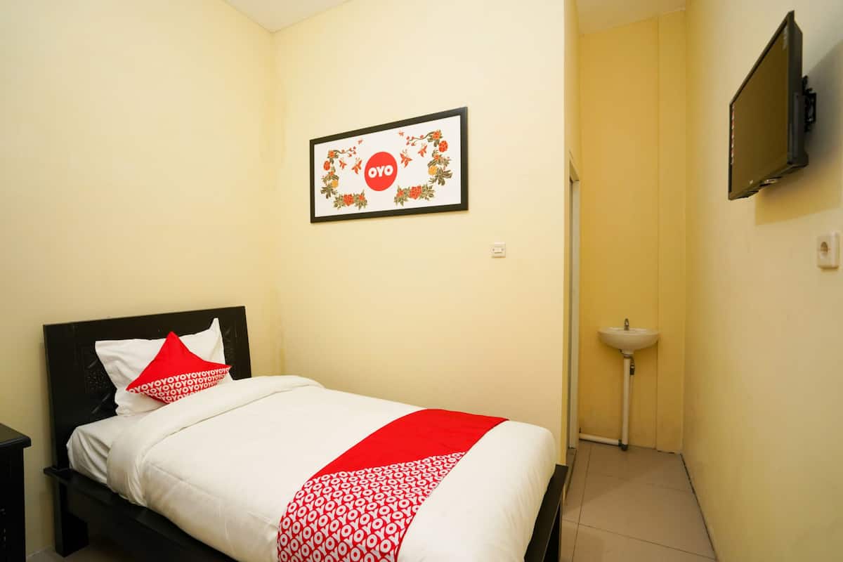 Una cama bien tendida con una colcha roja y blanca, un cabecero negro y un cuadro con un diseño floral en la pared.