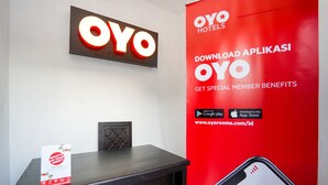 A reception desk with a sign for OYO Hotels, a digital clock, and a promotional poster for the OYO app. - OYO 998 La'ana Residence Syariah (Surabaya)