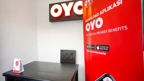 A reception desk with a sign for OYO Hotels, a red promotional banner, and a smartphone displaying a map. - OYO 998 La'ana Residence Syariah (Surabaya)
