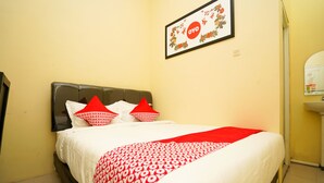 A neatly made bed with a red and white patterned bedspread, two red pillows, and a framed picture on the wall above. - OYO 998 La'ana Residence Syariah (Surabaya)