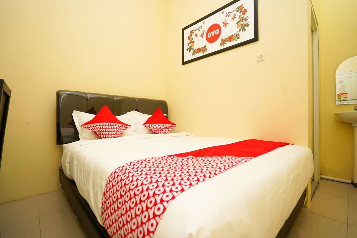 Una cama bien hecha con una colcha de diseño rojo y blanco, dos almohadas rojas y un cuadro en la pared de arriba.