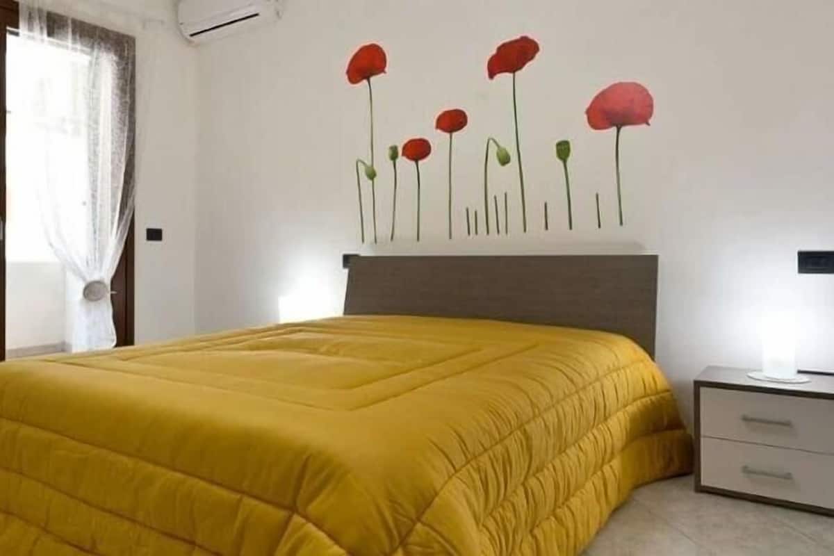 A room with a bed, a nightstand, a TV mounted on the wall, and a window with curtains.