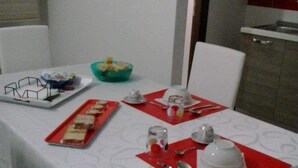 Ein Esstisch ist mit roten Platzsets, einer weißen Tischdecke und verschiedenen Geschirrteilen gedeckt.