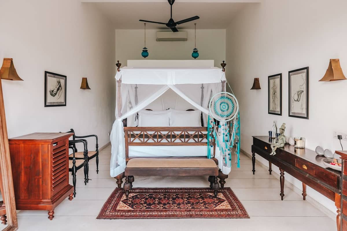 A bedroom with a four-poster bed, a wooden dresser, a desk, and a patterned rug.