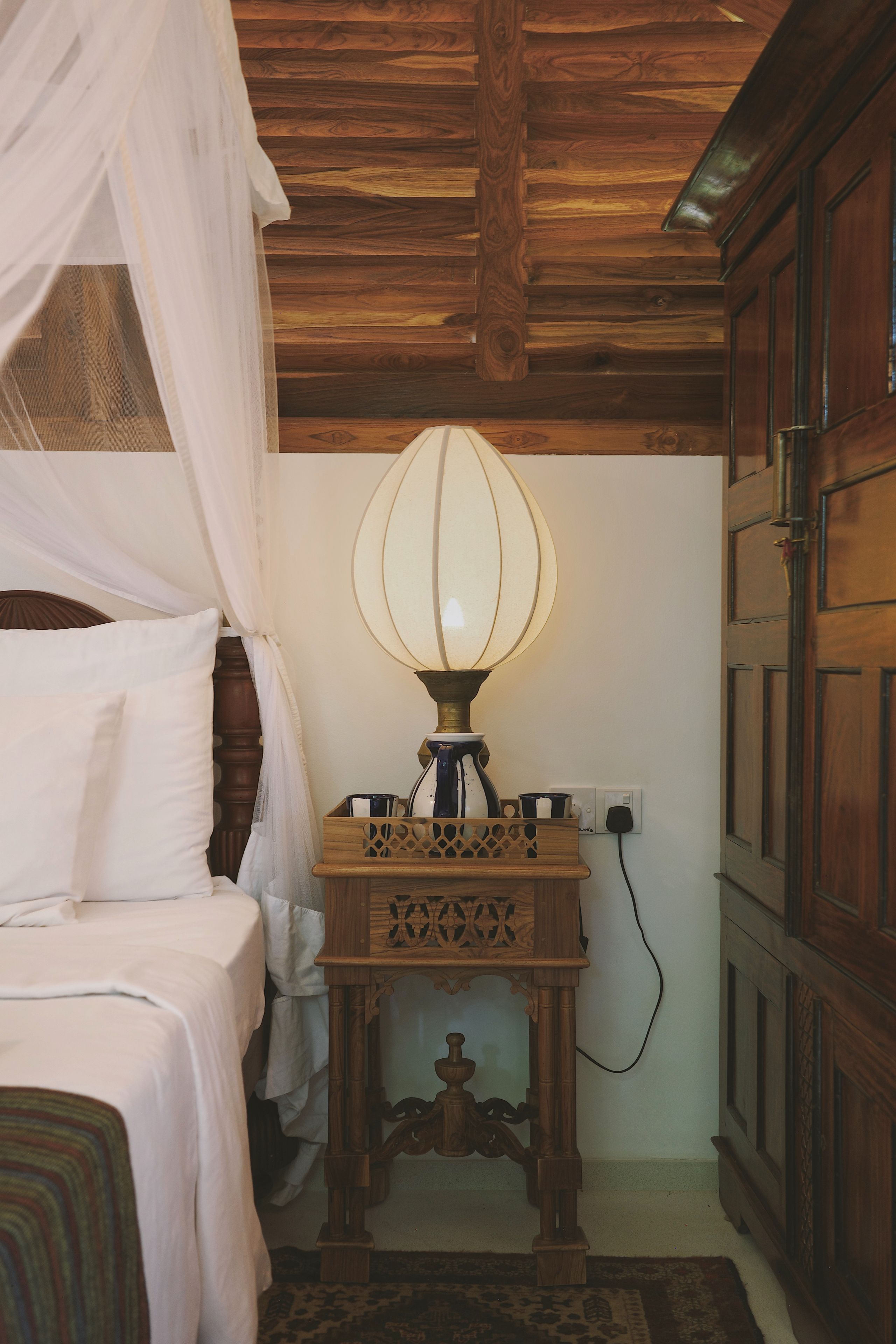 A bedroom with a bed, a bedside table with a lamp, and a wardrobe.
