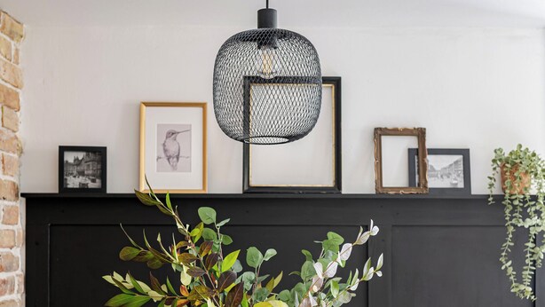 Un coin repas avec une table en bois, des chaises en métal, un vase avec des plantes vertes, une suspension noire et des tableaux encadrés accrochés au mur.