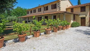 A large, two-story building with a tiled roof and multiple windows. There is a covered patio area with potted plants and a gravel driveway. - Villa Beboli per 18 pax by Interhome (Vinci)