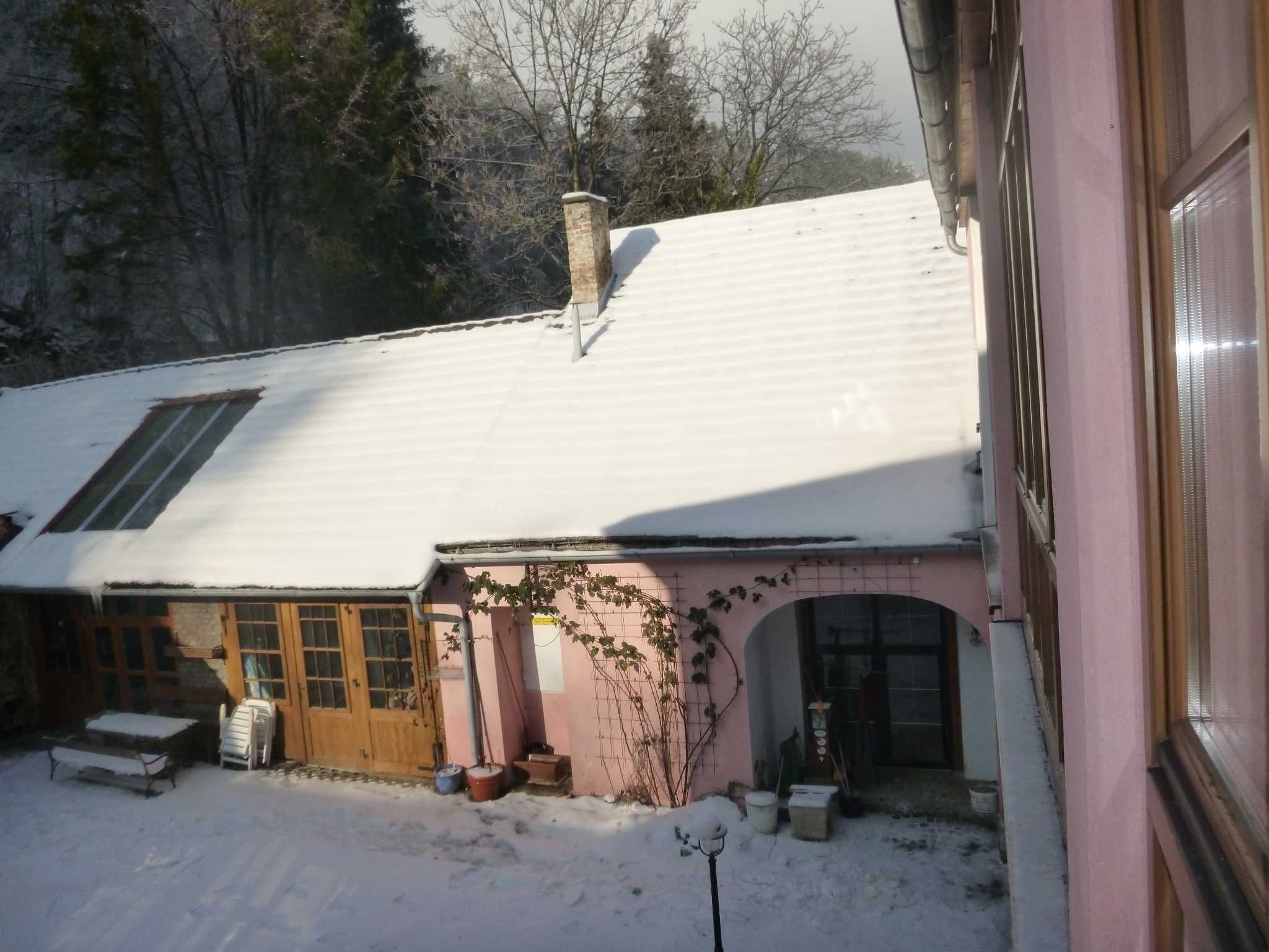 A snow-covered house with a chimney, wooden doors, and a small porch area.