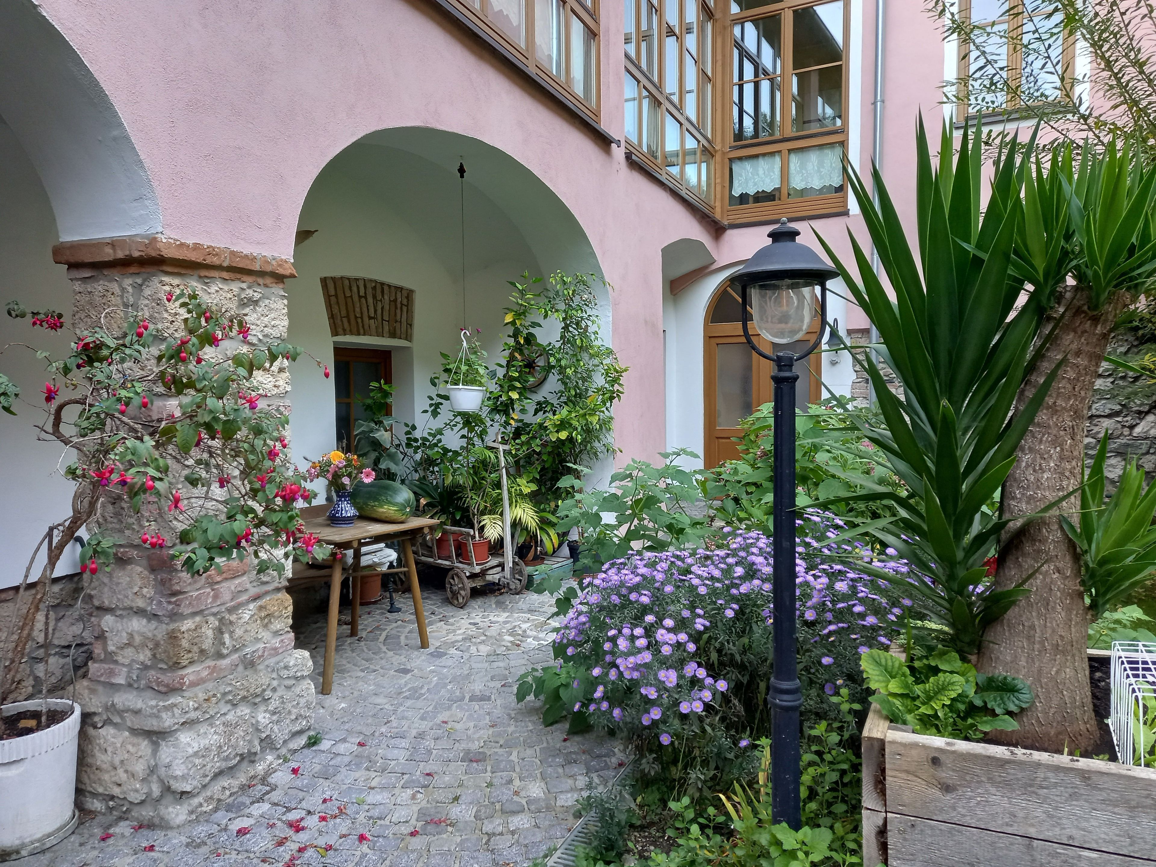 Une cour avec un sol en pierre, des plantes en pot, une table décorée de fleurs et un lampadaire.