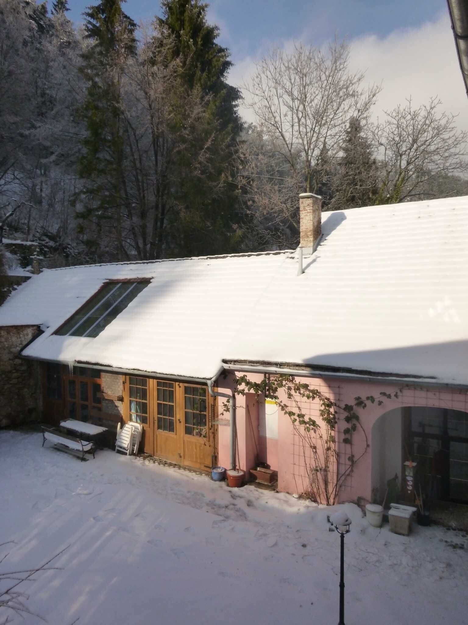 Ein mit Schnee bedecktes Haus mit geneigtem Dach, Schornstein und einer kleinen Veranda.
