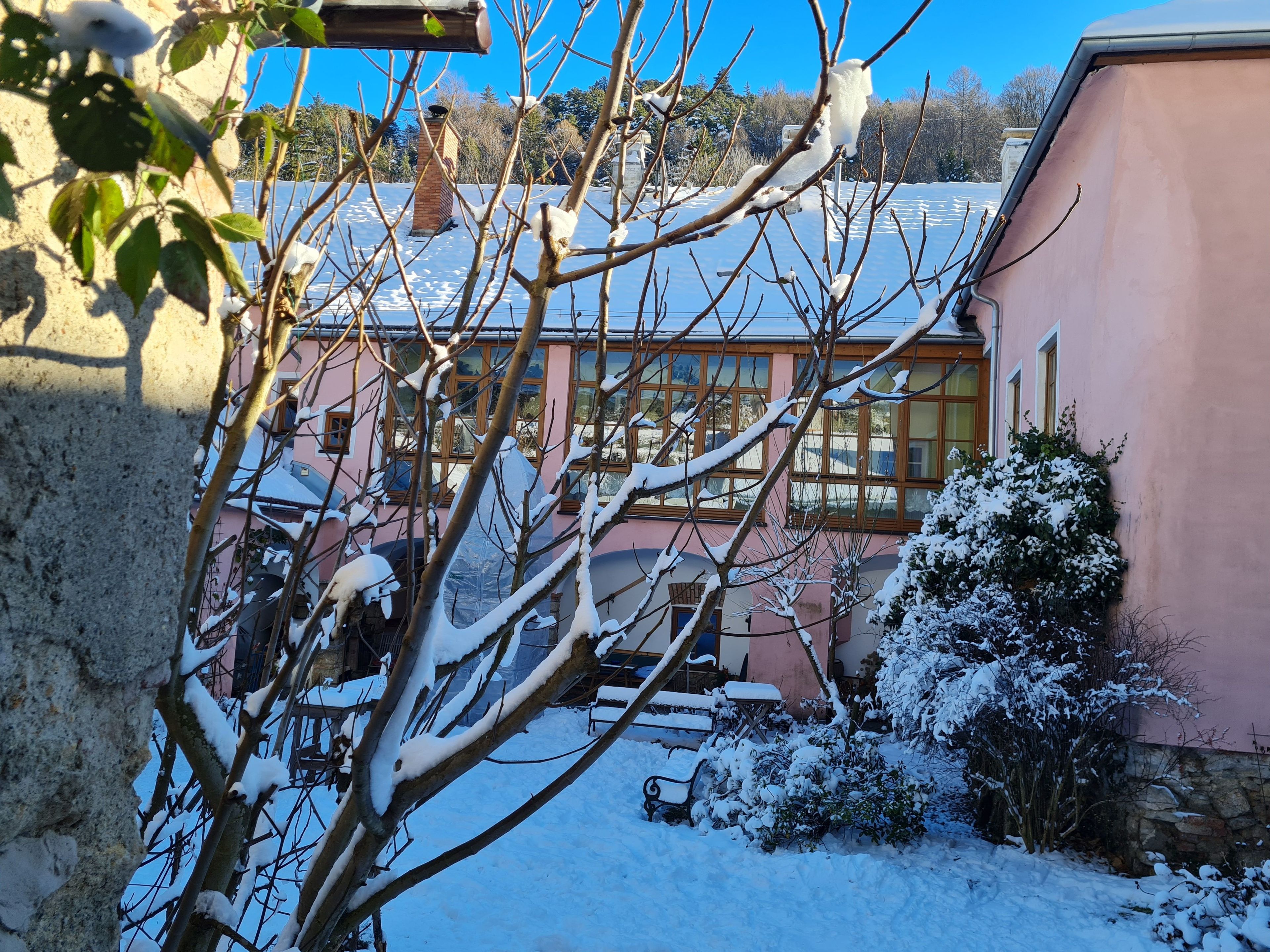 Ein rosafarbenes Gebäude mit schneebedecktem Dach, einer Steinmauer und einer Bank im Vordergrund.