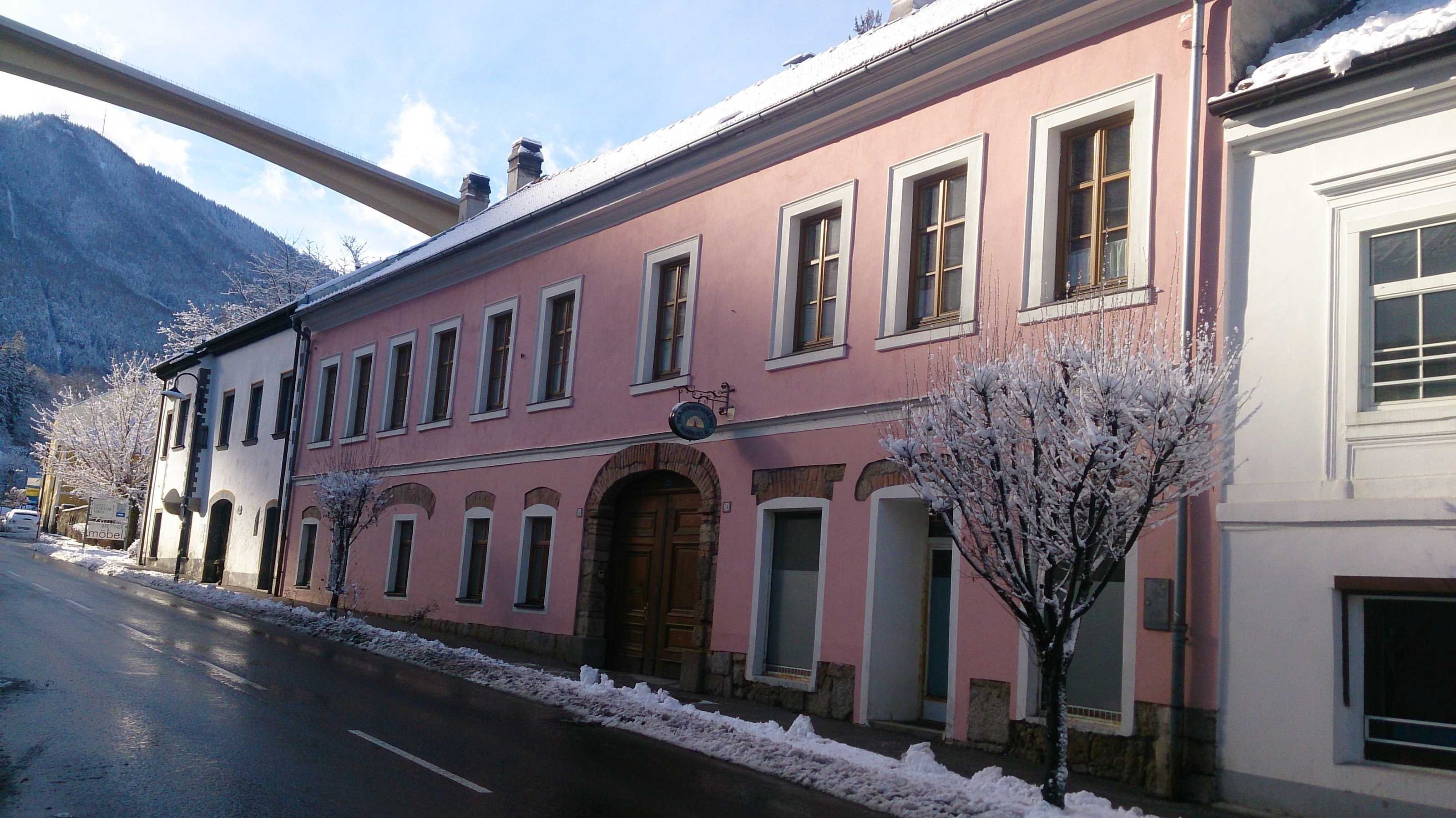A pink building with a central arched entrance, multiple windows, and a sign above the entrance.