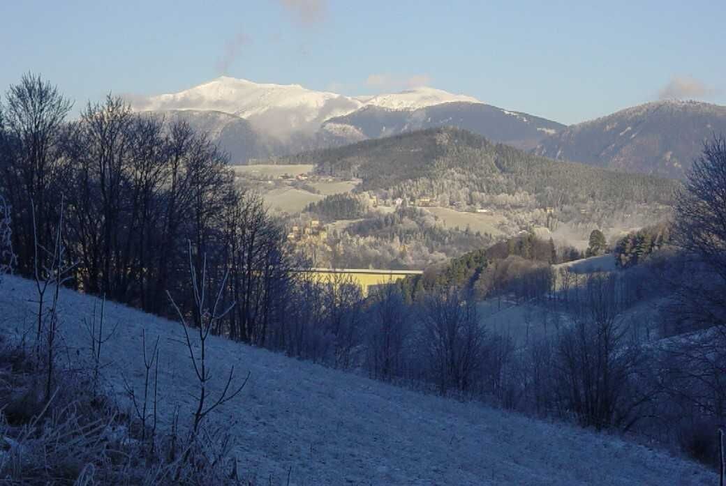 Schneebedeckte Landschaft mit Bergen im Hintergrund und blauem Himmel.