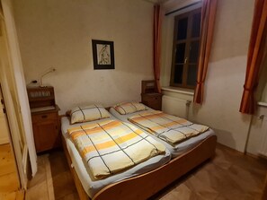A bedroom with a double bed, two bedside tables, a window with curtains, a radiator, and a wall-mounted picture. - Apartment 2 1 - Apartments Manuela (Breitenstein)