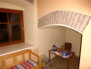 Una habitación con un banco de madera, una mesita con un reloj, una silla y una ventana con vistas.
