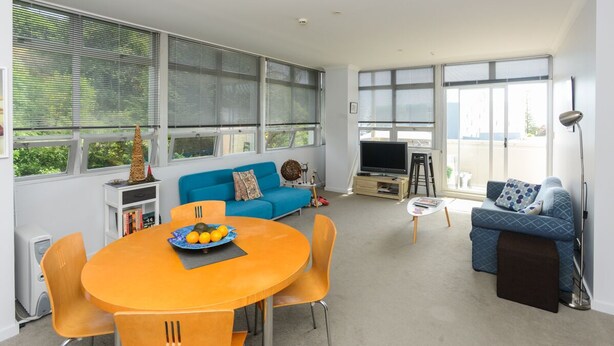 Una sala de estar moderna con una mesa redonda naranja, sofás azules y ventanas amplias.