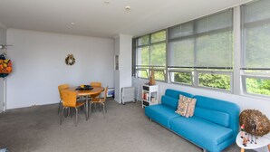 Una sala moderna con un sofá azul, una mesa de comedor con sillas y ventanas grandes con persianas.