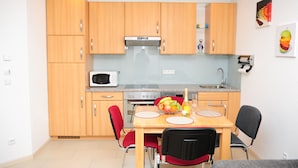 A compact kitchen with wooden cabinets, a microwave, a gas stove, and a dining area with a table and chairs. - Family-friendly apartment. Right in Tettnang. With terrace. Own parking lot. (Tettnang)