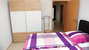 A bedroom with a bed, a wardrobe, a chair, and a door leading to another room. - Family-friendly apartment. Right in Tettnang. With terrace. Own parking lot. (Tettnang)