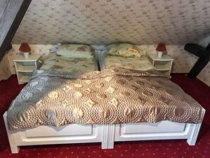 Un lit double avec une couverture à motifs, deux tables de chevet avec des lampes, un papier peint à fleurs et une moquette rouge.