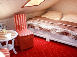A bedroom with a sloped ceiling, a bed with a patterned blanket, a striped chair, a small round table with a vase, and a red polka dot carpet. - Zielona Dolina Młyn by Interhome (Kwilcz)