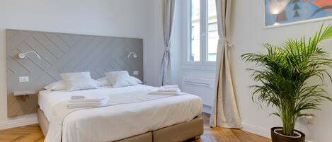 Un dormitorio moderno con una cama grande, un cabecero con diseños geométricos, una planta en maceta y un cuadro en la pared.