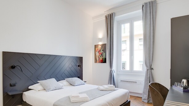 A modern bedroom with a large bed, a desk, and a window with curtains. - The Right Place (Rome)