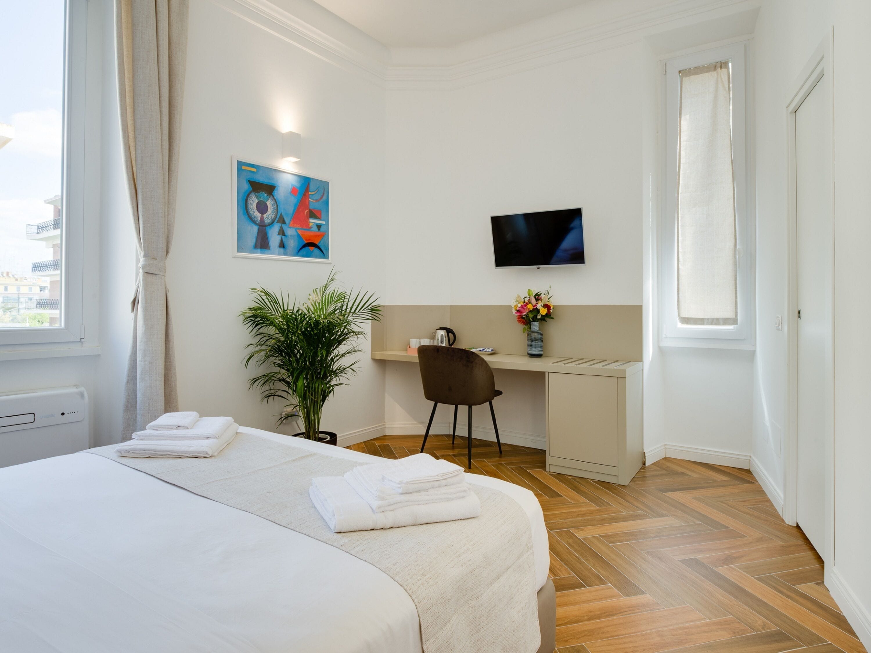 Habitación de hotel con cama, escritorio, silla, televisor, planta y ventana.